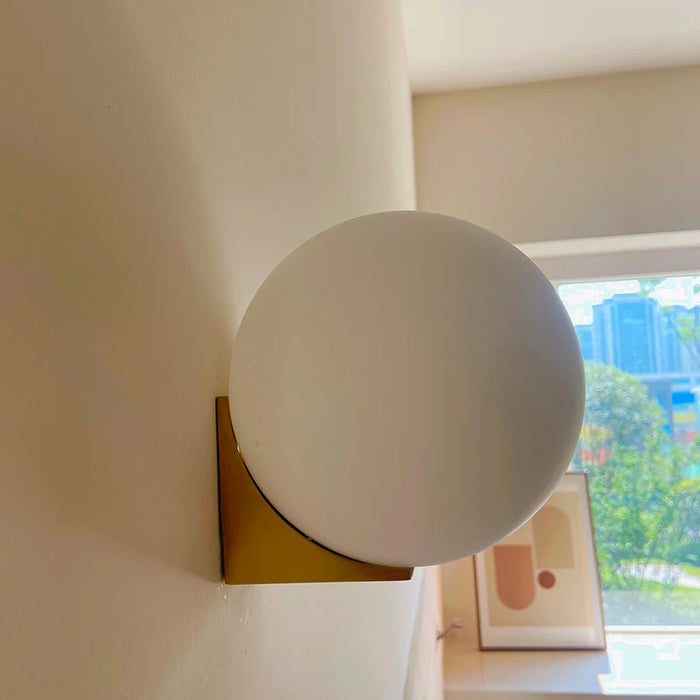 Solja – minimalist glass orb wall sconce in a bedroom corner – gold finish with frosted globe